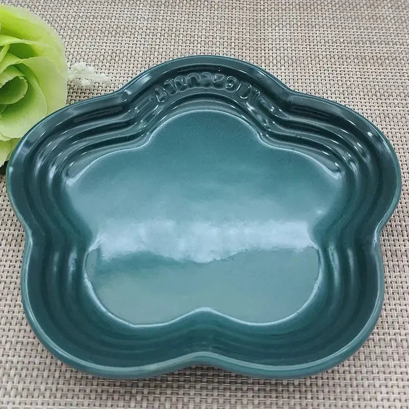 Teal ceramic pet bowl with scalloped edges, ideal for dog or cat food and water, placed on woven mat with green flower accent.